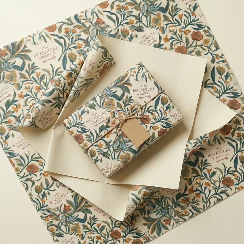 A small gift wrapped in floral repeat wrapping paper and tied with twine and a kraft tag, on printed sheets of the same paper